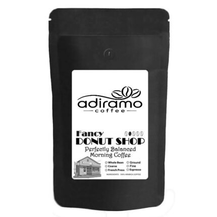 A 1lb black pouch of Adiramo Fancy Donut Shop Perfectly Balanced Morning Coffee on a wooden table near a steaming mug and pastry.