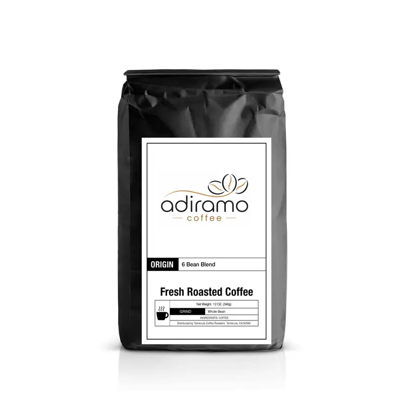 Adiramo 6 Bean Blend 12oz black coffee bag with white label standing next to a steaming mug and fresh roasted whole coffee beans